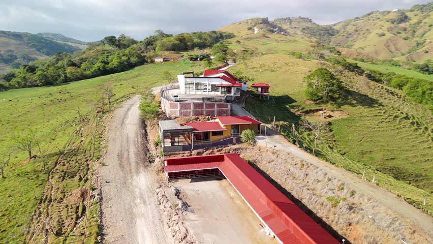 Stunning aerial perspective circling a modern farmhouse and barn built on a scenic hillside, surrounded by lush green mountains and a beautiful natural landscape on a sunny day in the countryside