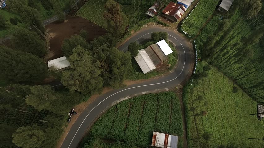 4K top down drone shot of a winding road through misty green terraced fields.