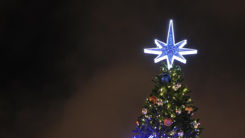 Christmas tree with glowing blue star topper against dark night sky
