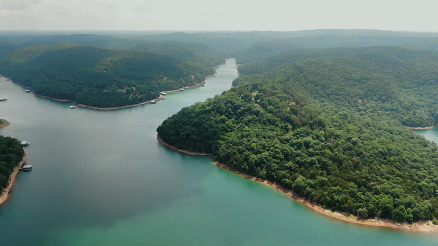 Aerial shot of the winding Beaver Lake in Arkansas, showcasing vibrant blue water and dense green forest hills. High quality nature landscape for travel and environmental content.