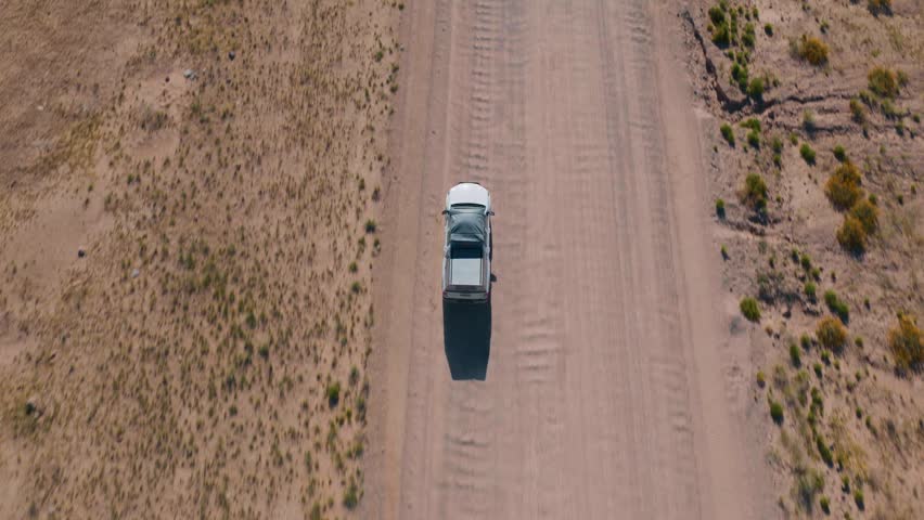 Aerial view of a 4x4 vehicle traveling on a long, straight dirt road through the vast, arid landscape of Namibia, representing adventure travel, tourism, and exploration of wild nature