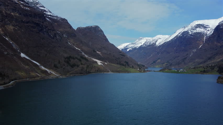 Aerial view of a deep Norwegian fjord with snow-capped mountains and small settlements along the shoreline.