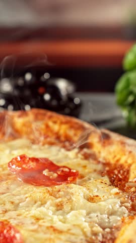 Super slow motion footage (1000 fps) of a pizza slice being lifted with perfectly melted, stretchy cheese. Rich textures of crust, salami, tomato and fresh basil in cinematic light.