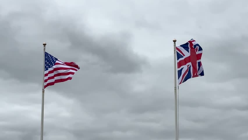 American and British flags waving on the cloudy sky