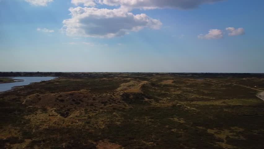 A wide view shows a landscape with a river flowing through land formations under a clear sky with clouds. The natural environment showcases land and water together.