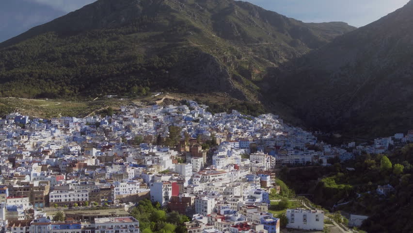 High drone pullback over Chefchaouen blue city encircled by Rif Mountains