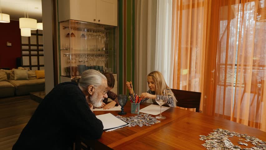 Grandfather watches his two granddaughters draw while they sit at the table