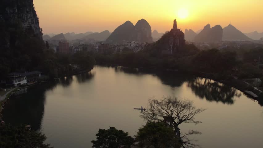 A serene sunset landscape featuring a calm lake, karst mountains, and a pagoda silhouette in natural scenery.
