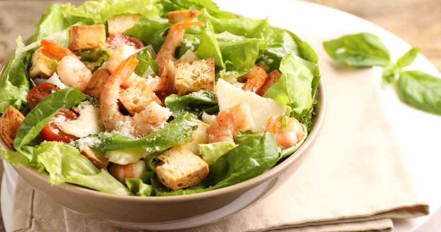 Delicious Caesar salad with shrimps in bowl on table, closeup