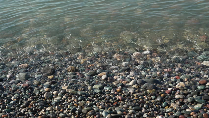 Close-up of a wave washing over gravel beach. The sea water rolls over and washes the pebble beach