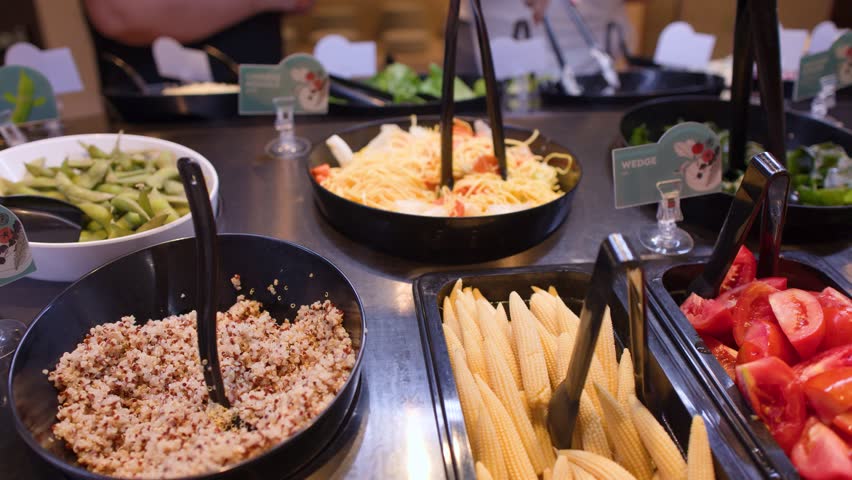 A high-angle panning shot across a vibrant salad bar buffet with fresh vegetables and grains.