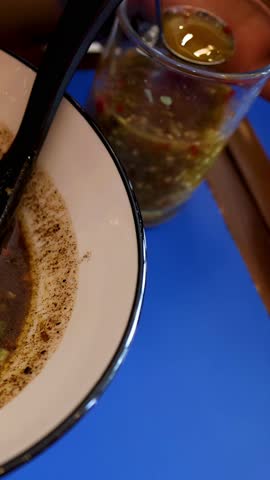 A close-up shot shows spicy chili sauce being poured into a bowl of pork noodles.