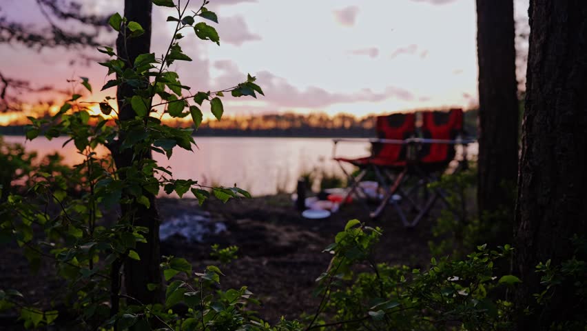 Soft sunset light over quiet lakeside campsite with fading campfire embers