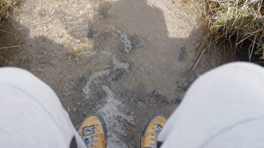 Clear mountain stream flowing through grassy terrain with patches of melting snow