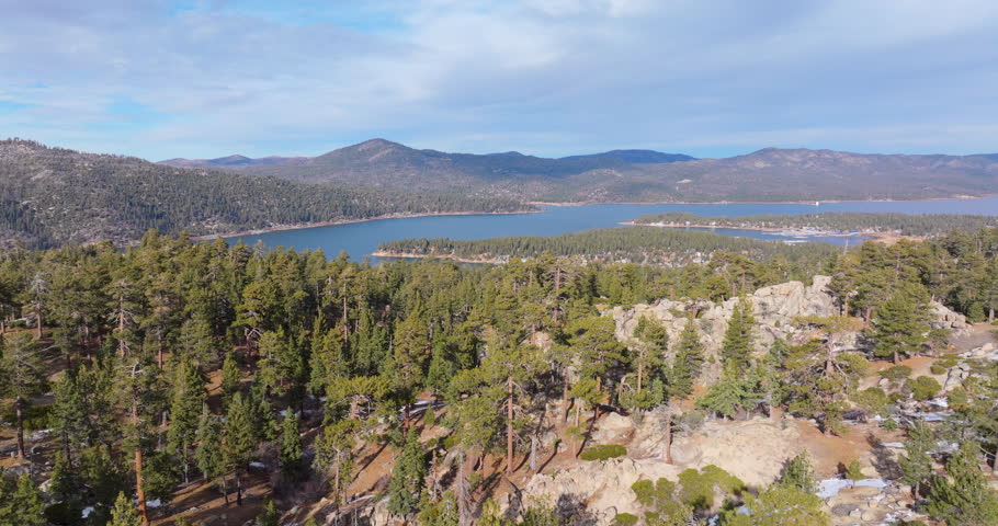 Flying over pine forest revealing lake and mountains