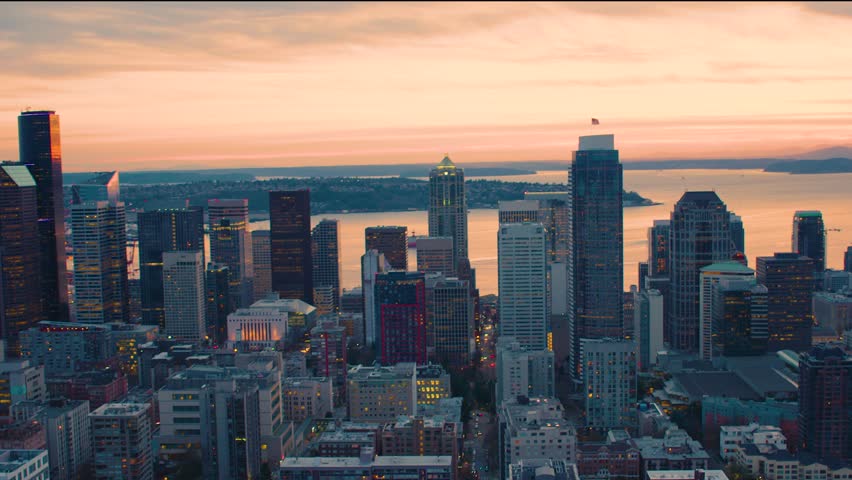 Panoramic view of downtown Seattle skyline at dusk, glowing skyscrapers, aerial perspective, urban landscape, water views, cinematic drone footage.