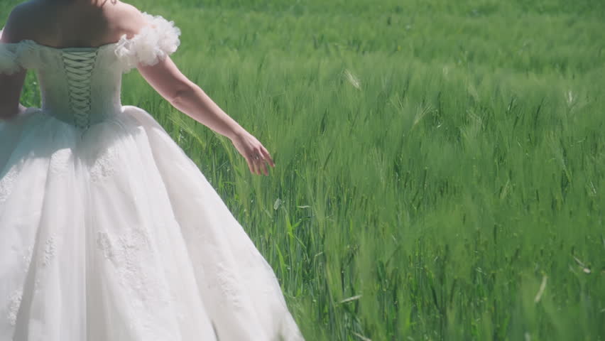Bride with white wedding dress walking in field with hand touching the grass, outdoor, gimbal shot