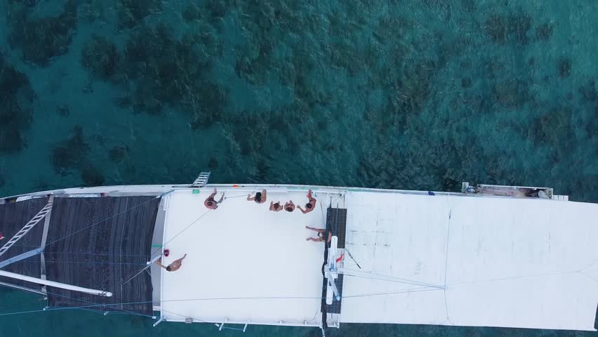 Amazing aerial view of a group of friends having fun jumping from the deck of a boat into the beautiful turquoise sea in indonesia