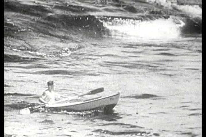 1950s - Boats fight big waves near a beach.