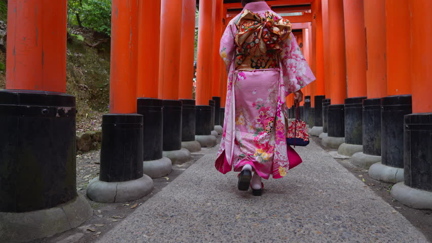Asian woman in traditional Japanese kimono at Fushimi Inari Shrine in Kyoto Japan.And there is an inscription on the pillar: “Dedicated as an offering to a Shinto shrine.”