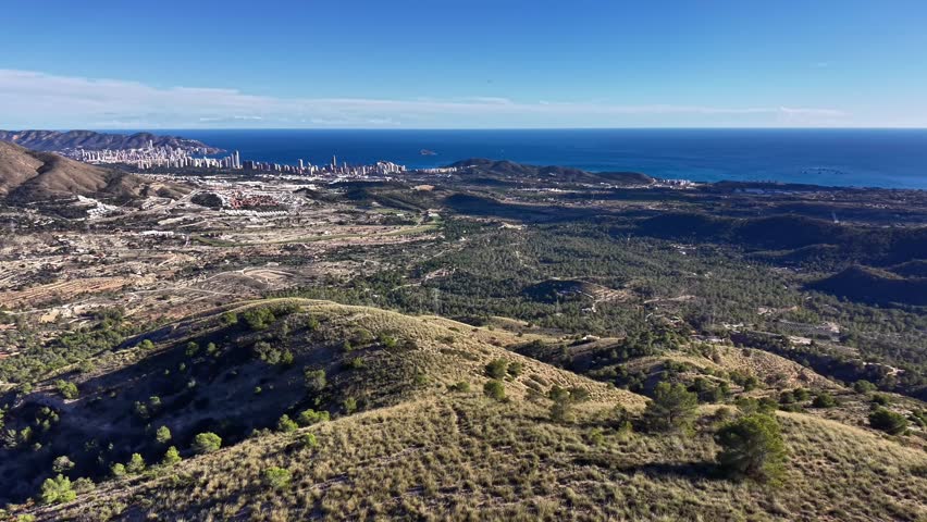 Aerial hills overlooking sea and skyline, sunlit scrubland and rolling ridges, scattered pine clusters,