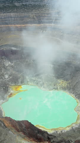 Aerial drone view of a turquoise crater lake inside a volcanic crater in Guatemala, surrounded by rugged volcanic rock formations and geothermal landscape. Vertical