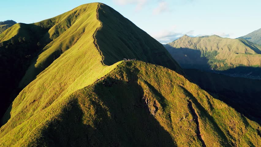 Hikers gather on a scenic mountain Trail surrounded by steep green volcanic hills and golden early morning light in Lombok Indonesia, push-in aerial drone footage