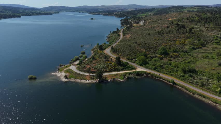 Winding road curves along vast Douro reservoir scrubland shoreline with rocky points islands and distant hills