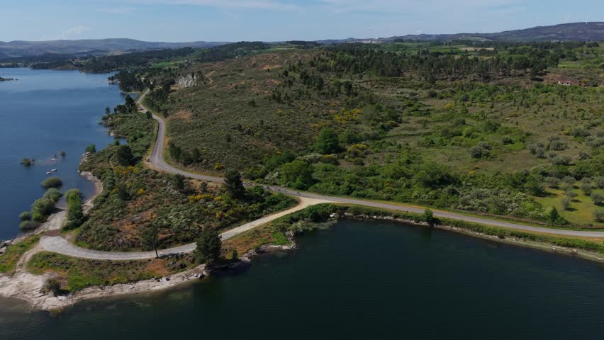 Winding road curves along Douro reservoir scrubland peninsula with rocky shoreline islands and rolling hills