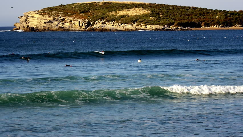 Santander, Cantabria, Spain, March 3 2025: Surfers paddle, waiting for breaking ocean waves. Coastal landscape with a headland in a tranquil water sports scene