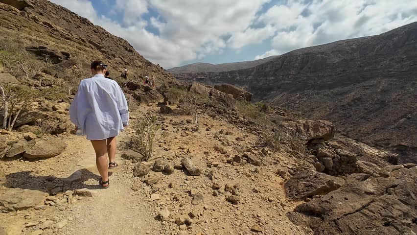 hikers walking along a rocky mountain trail in a dry desert landscape under a cloudy sky. Socotra, Yemen.