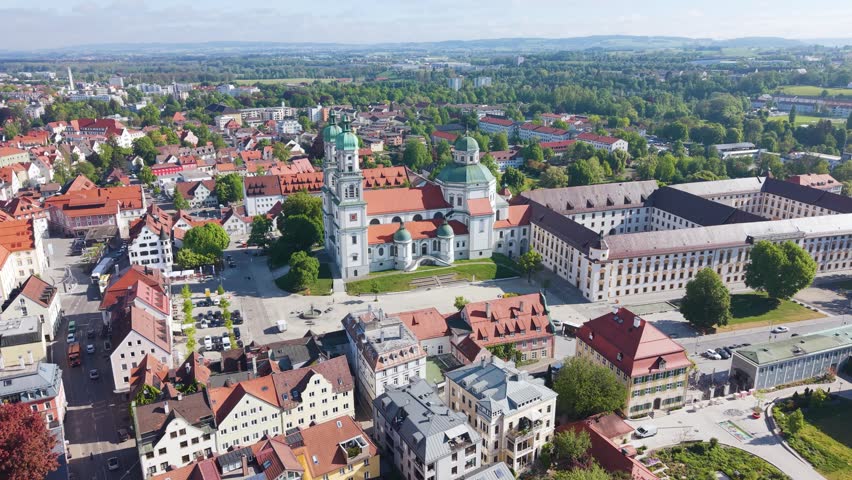 Orbiting aerial shot of Basilica Saint Lorenz Church in Kempten Allgäu, Germany, featuring historic architecture, red rooftops, and the surrounding town square in Bavaria. UHD.