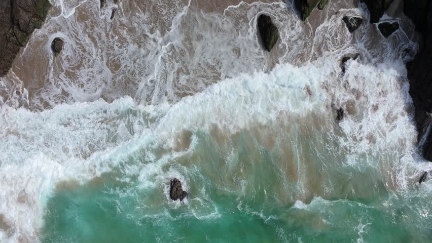 Waves create dynamic patterns as they meet the rocky shoreline and sandy beach. Ideal for travel and nature projects.