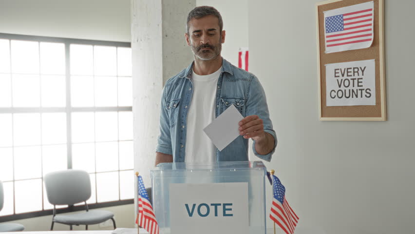 Man places ballot into transparent ballot box with hand visible in voting building; civic responsibility.