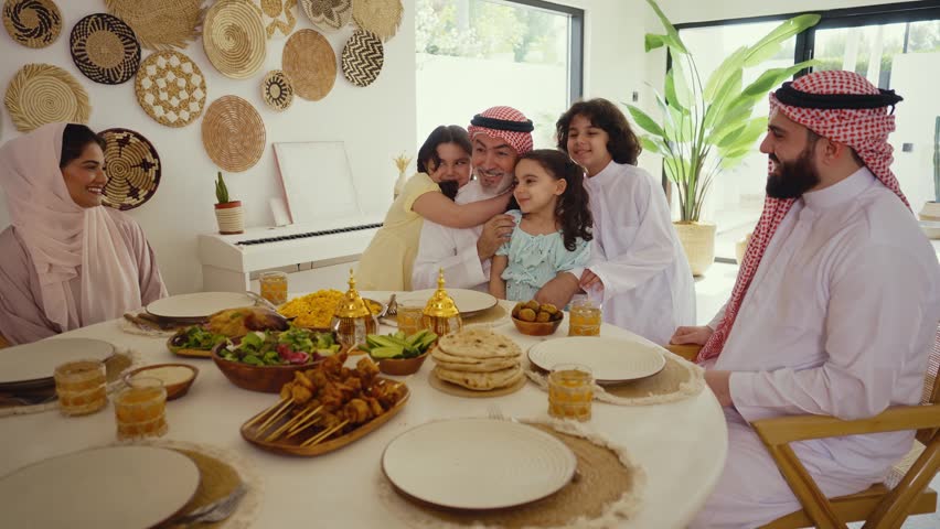 Arab family wearing traditional saudi clothing having lunch at home - Middle-eastern family bonding and having fun on a family reunion dinner