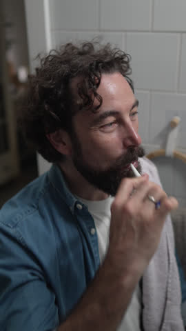 Handsome caucasian man with a beard and curly hair brushing his teeth with a toothbrush in the bathroom. Dental health, oral hygiene, and daily morning routine for a fresh clean mouth