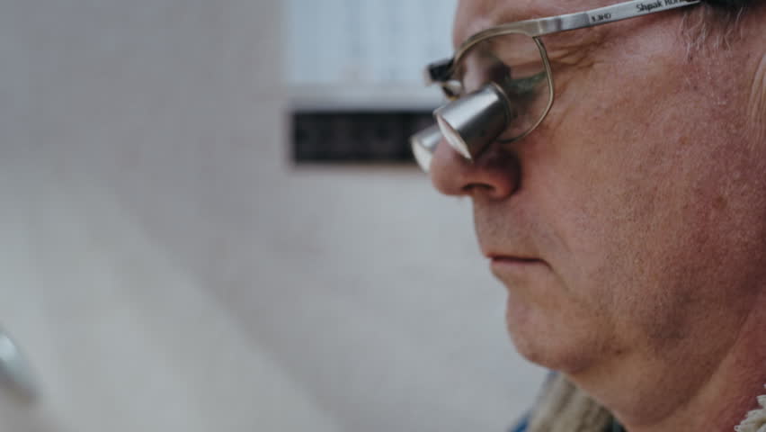 A lab specialist wears binocular loupes while shaping a false crown, bringing the restoration inches from his eyes.