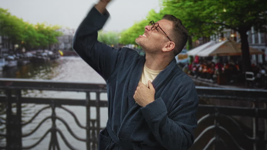 Man in robe raises hands and looks up on a street bridge, covering ears and grimacing; frustration solitude.