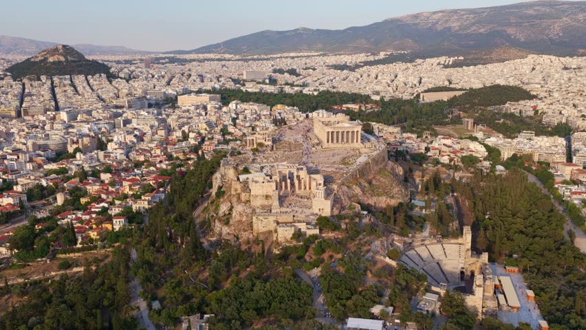 Majestic aerial view flying over the acropolis of athens, showing the parthenon, the propylaea, and the odeon of herodes atticus, with the sprawling city and mount lycabettus in the background