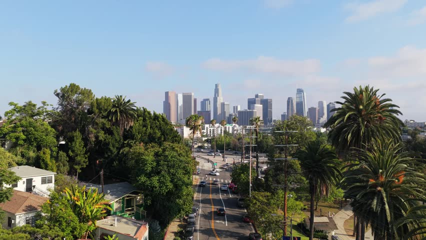 Urban landscape showing Downtown Los Angeles skyline with palm tree lined streets and busy traffic moving forward on a sunny day in Southern California