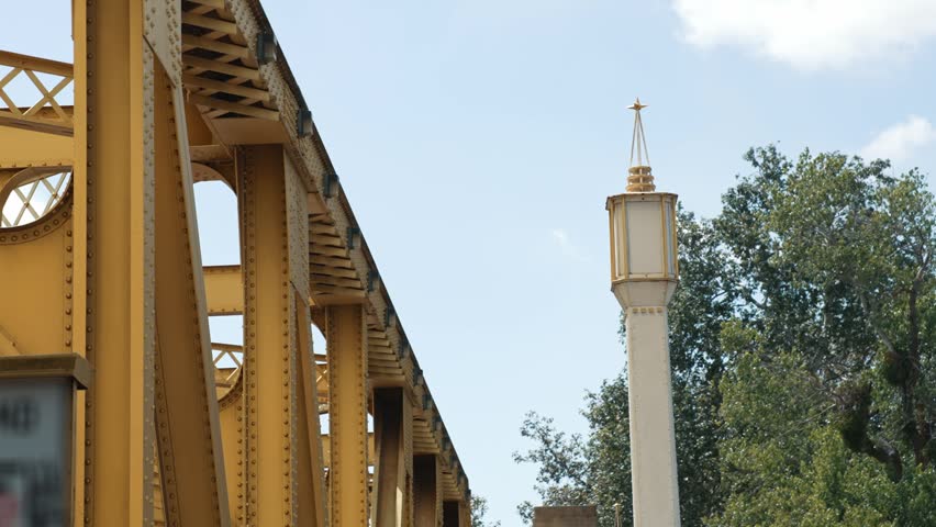 Historic lamp beside the golden bridge in Sacramento against a blue sky and green trees on a sunny day near the urban waterfront