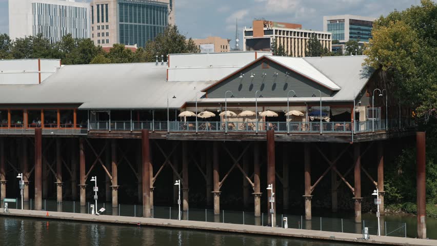 Historic stilt building along the Sacramento waterfront with a terrace and views of the modern downtown skyline beside the river on a sunny day