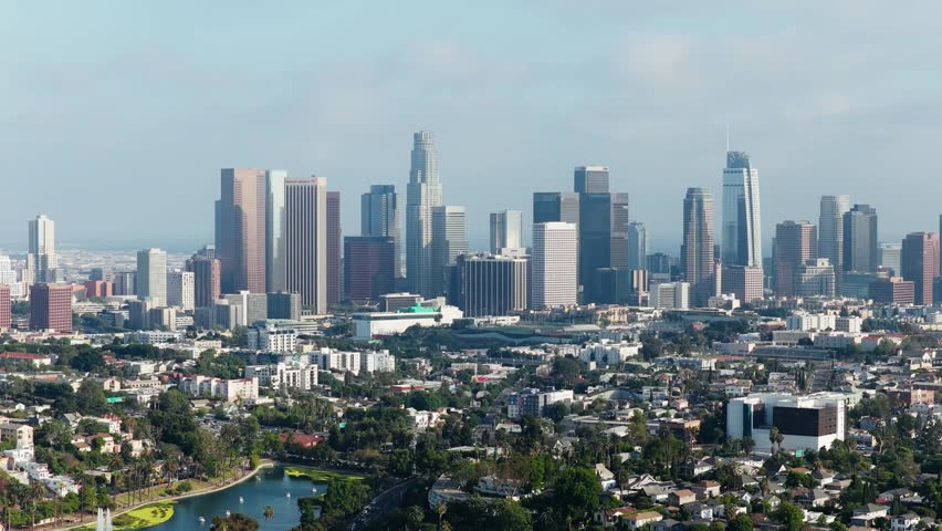 High angle panoramic flying towards downtown Los Angeles skyline, financial district skyscrapers and Echo Park Lake urban landscape during sunny day in California