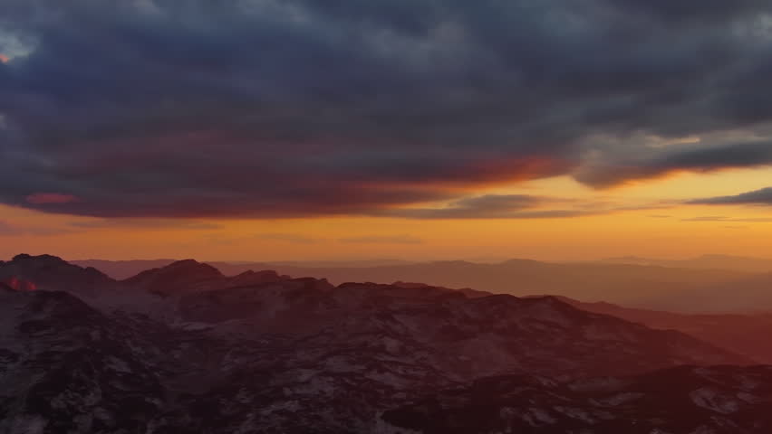 Orange sun setting over mountain with dramatic clouds. Evening sky at sunset with orange light, aerial view, panorama 4k