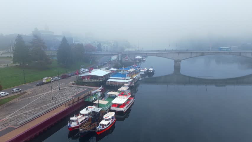 Flyover between tourist boats moored along the waterfront in Valdivia, Chile, on a morning with thick fog