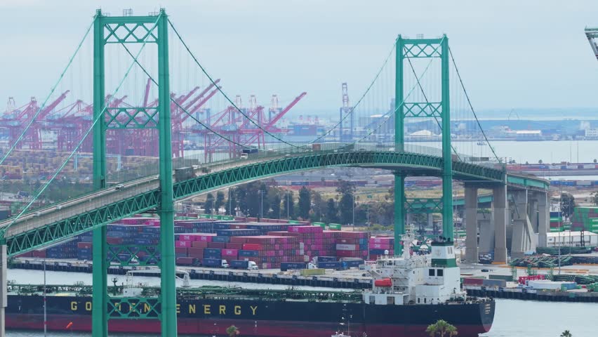 Traffic crossing Vincent Thomas Bridge over Los Angeles harbor with cargo ship, containers, cranes showing busy commercial activity at Port of Los Angeles