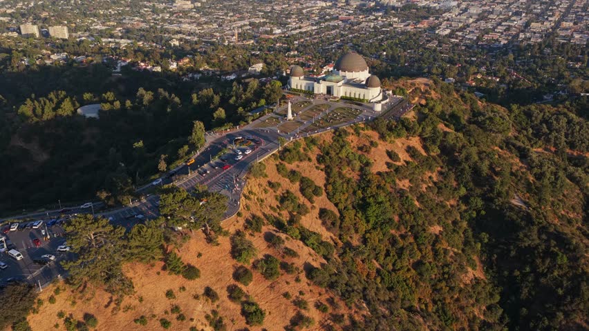 Cinematic tilt of Griffith Observatory on Hollywood Hills with Downtown Los Angeles skyline, Griffith Park, California, USA landmark during a sunny day