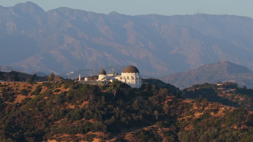Griffith Observatory perched on a hill with San Gabriel Mountains in background during sunrise in Los Angeles, California showing amazing science location