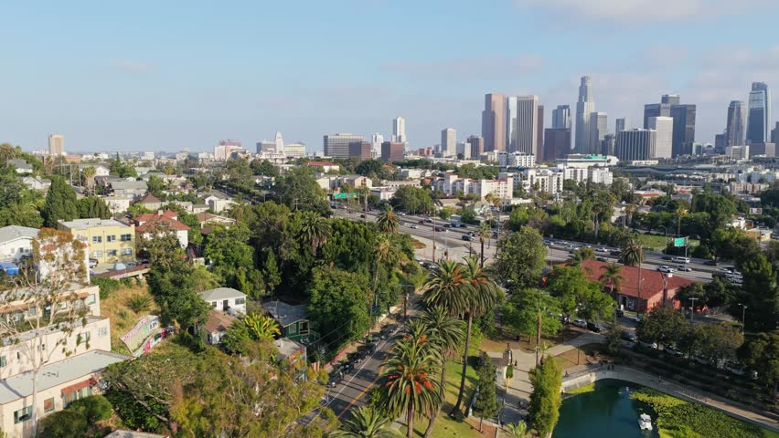 Scenic landscape of Echo Park Lake and downtown Los Angeles skyline with freeway traffic and lush palm trees on sunny afternoon in southern California