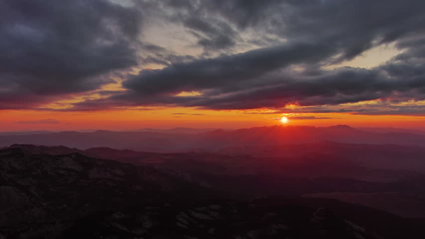 Orange sun setting over mountain with dramatic clouds. Beautiful evening sky at sunset with orange light, aerial view 4k